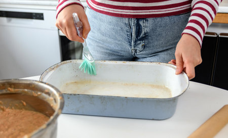 Midsection image of woman using kitchen utensil to grease a cake pan. Person cooking and baking in kitchen at home.の写真素材