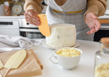 Close-up image of woman baking and decorating cake. Woman using spatula to apply white icing or frosting on a cake.の写真素材