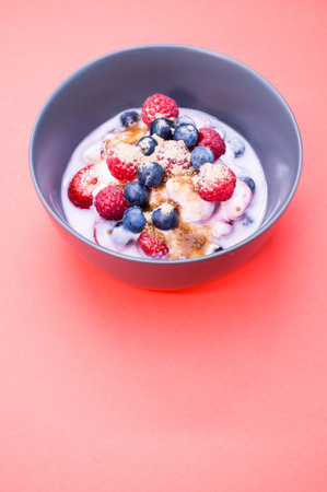 A bowl of yogurt with raspberries, blueberries, and powder isolated on red backgroundの写真素材