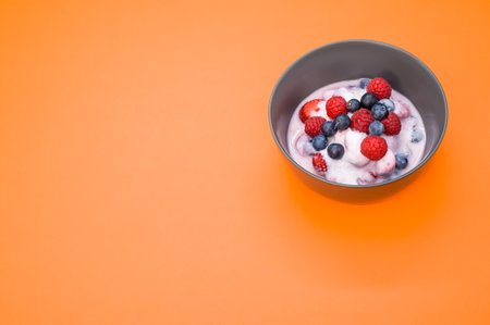 A top view of yogurt with fresh raspberries and blueberries on a bowl isolated on orange backgroundの写真素材