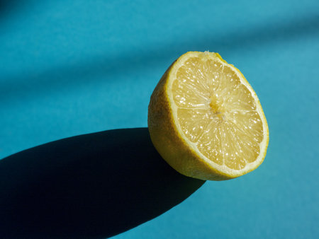 A closeup shot of fresh half cut juicy lemon on a blue surface under a bright sunlightの写真素材