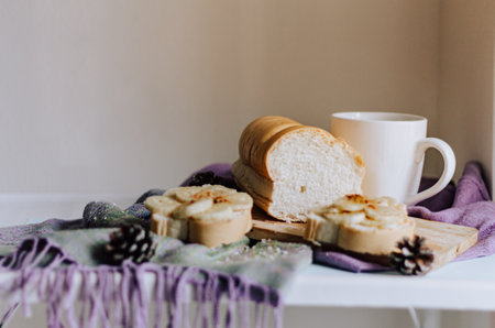 A shot of a breakfast table with banana toasts, bread, and a mug of coffee under the sunlight