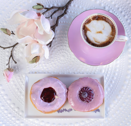 A top view of two pink donuts, a cup of coffee and orchids on a white surの写真素材