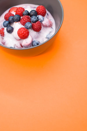 A vertical shot of yogurt with raspberries and blueberries on a bowl isolated on orange backgroundの写真素材
