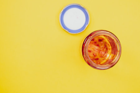 A top view of an open empty strawberry jam jar with lid isolated on light yellow backgroundの写真素材