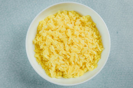 A closeup shot of a bowl of boiled rice on a turquoise surface