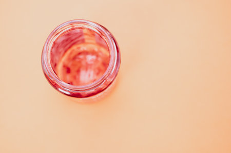 A top view of an empty strawberry jam jar isolated on peach background