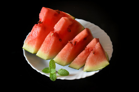 A fresh red watermelon slices on a white plate isolated on black