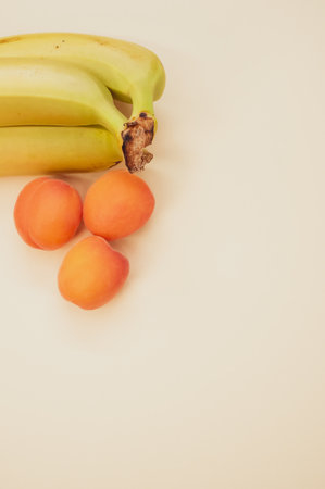 A vertical shot of ripe bananas and apricots isolated on light brown backgroundの写真素材