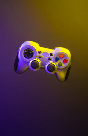 Game console controller levitating against a multi-colored illuminated background. International day...