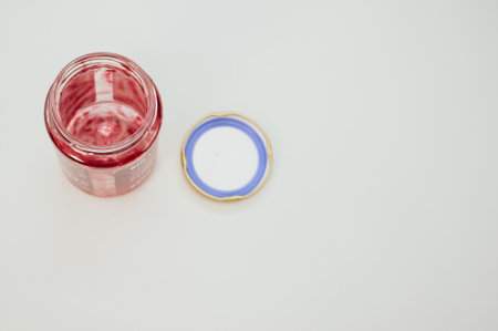 A high angle shot of an open empty strawberry jam jar with lid isolated on light gray backgroundの写真素材