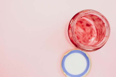 A top view of an open empty strawberry jam jar with lid isolated on light pink backgroundの写真素材