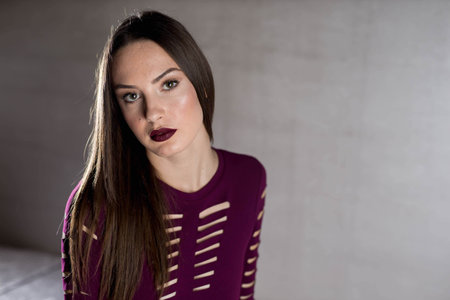 An attractive Caucasian female wearing a burgundy dress posing in a room
