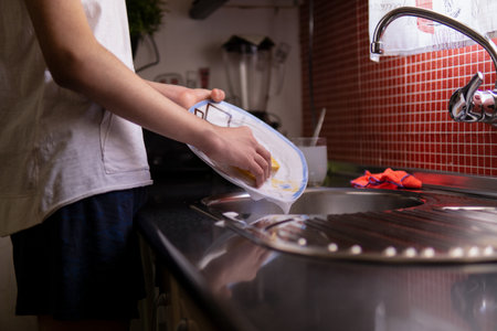 Teenager boy washing dishes at homeの写真素材