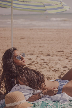 Vertical camera position of a black girl lying on the beach as she sunbathes on a sunny day. Summer vibes concept 2021.の写真素材
