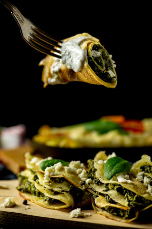 Crepes with spinach on the cutting board and fork, black tableの写真素材