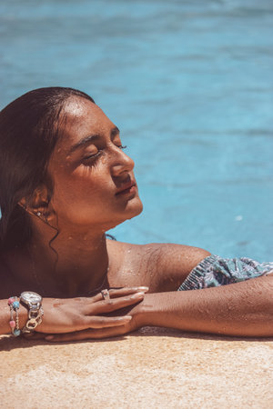 A relaxed and pensive black girl leaning against the pool of her flat while she looks to the side...