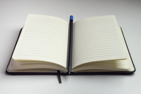 Opened notebook with empty white sheets with horizontal lines and a pencil with a white backgroundの写真素材