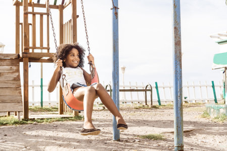 happy and smiling afro american girl playing on swing. fun and recreation concept.の写真素材