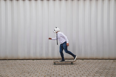 Businessman skateboarding on longboard with a panda bear mask against gray wallの写真素材