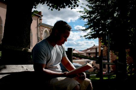 A latin man reading a book outdoors