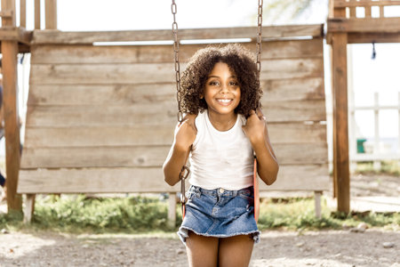 happy girl with afro hair Latin American ethnicity sitting on a swing. fun and recreation concept.の写真素材