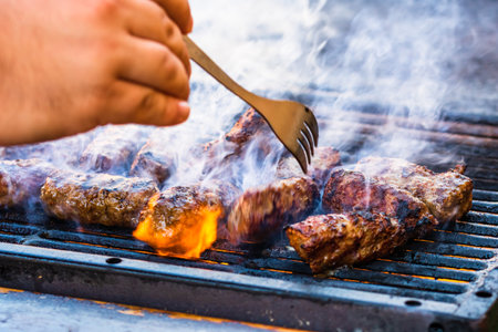 Preparing meat rolls called mici or mititei on barbecue. close up of grill with burning fire with flame and smoke.の写真素材