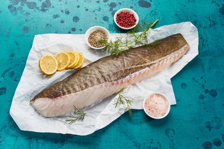 High angle of fresh fish fillet and various aromatic spices and herbs served on blue table in...