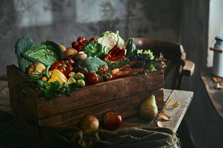 Harvest of assorted ripe fresh vegetables and fruits placed on wooden table in rustic houseの写真素材