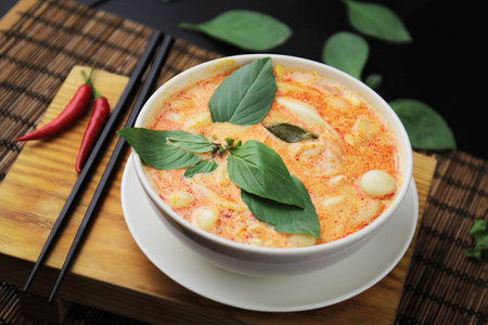 Red curry in a white bowl, chopsticks, black background