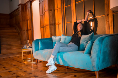 A young Caucasian woman sitting on a blue sofa enjoying herself in a traditional wooden houseの写真素材
