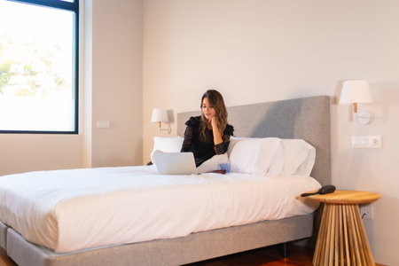 Young blonde Caucasian woman sitting on the bed at home watching online news and social networksの写真素材