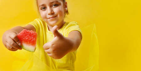 Caucasian girl out of focus on yellow background making ok gesture and holding a piece of watermelon. Concept of fresh and healthy fruit. Selective focus in foreground. Copy space.の写真素材