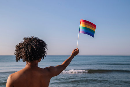 Young man with afro hair raises a pennant with lgtbi colorsの写真素材