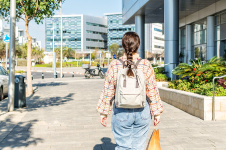 Young Caucasian woman, back view, walking down, the street with shopping bag, on a sunny autumn day....