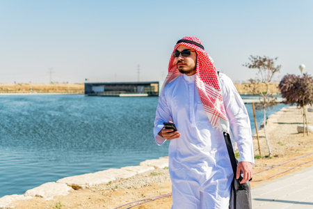 Front view of Saudi Arabian man, in traditional dress, walking in a maritime area.