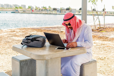 Side view of an arab saudi man working with a laptop in a maritime area.の写真素材