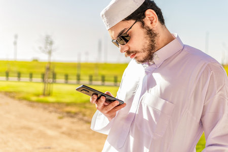 Portrait of an arab saudi emirates man using a smart phone, outdoor in a park.