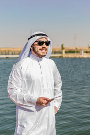 Happy Muslim man in traditional clothing, smiling at maritime zone, in Middle East.
