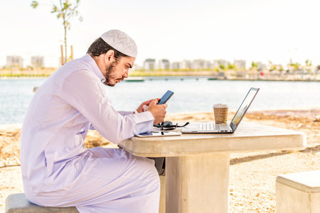 Arab man working on the phone and a laptop at maritime area in Middle East.の写真素材
