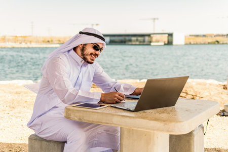 Happy islamic man working on the tablet and a laptop at maritime area in Middle East.の写真素材