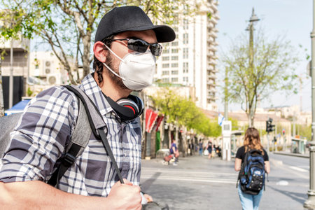 Young man with protective mask, backpack, on a city street.の写真素材