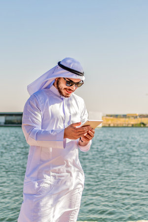 Portrait of happy Muslim man, in traditional clothes, checking content on a tablet, in the Middle East.の写真素材