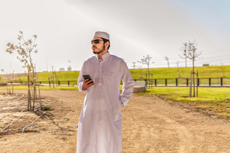 View of Arab man in traditional dress, with smart phone, looking into the distance, outdoors.