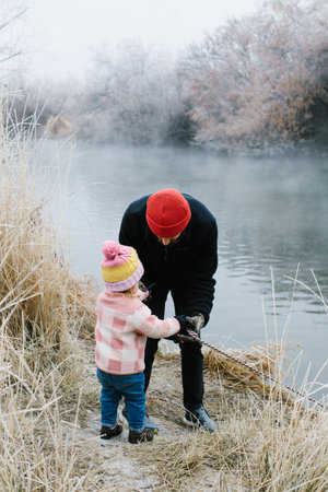 Little girl with her father and their dog walking on a greenbelt path next to a river on a cold winter dayの写真素材