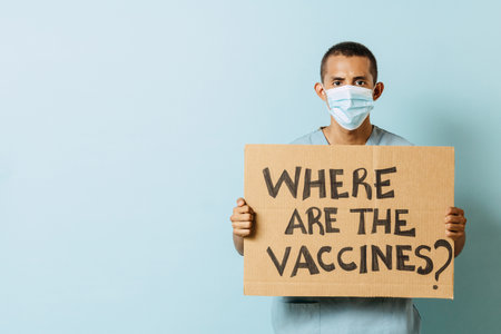 Young latinx health staff man holds a banner. Hispanic man nurse holds a sign. where are the vaccines.の写真素材