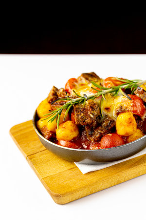 Meat with potatoes and vegetables in a frying pan, white background, copy spaceの写真素材