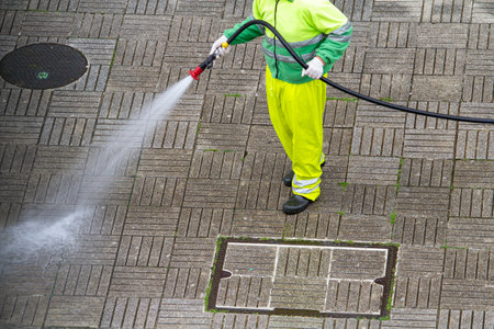 Worker holding a hose cleaning a sidewalk with water. Urban Maintenance or cleaning conceptの写真素材