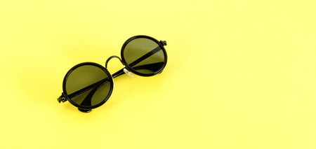 Stylish black sunglasses isolated on yellow background, top view. Summertime concept.の写真素材