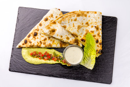 Quesadilla with chicken and sauce on a black plate, top view